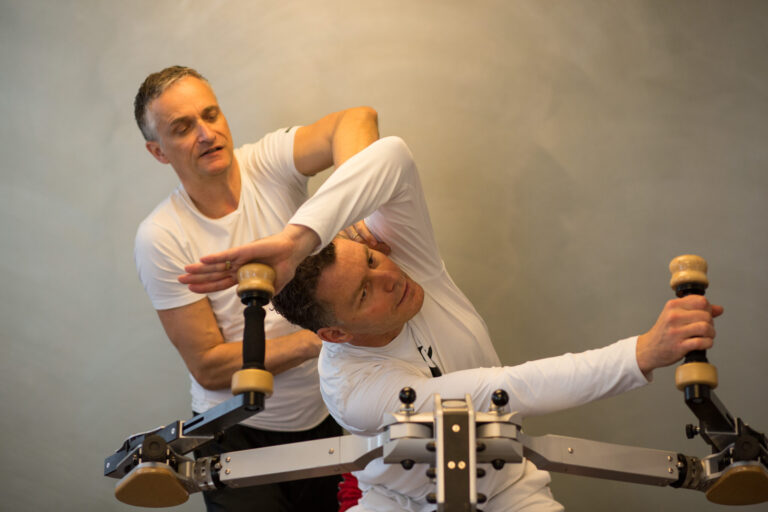 Trainer correcting a spiral movement on a client's back at the Gyrotonic machine.