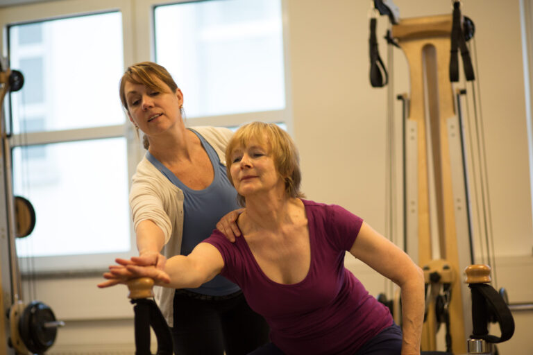 A trainer supports a client's arm position during an exercise on the Gyrotonic machine.