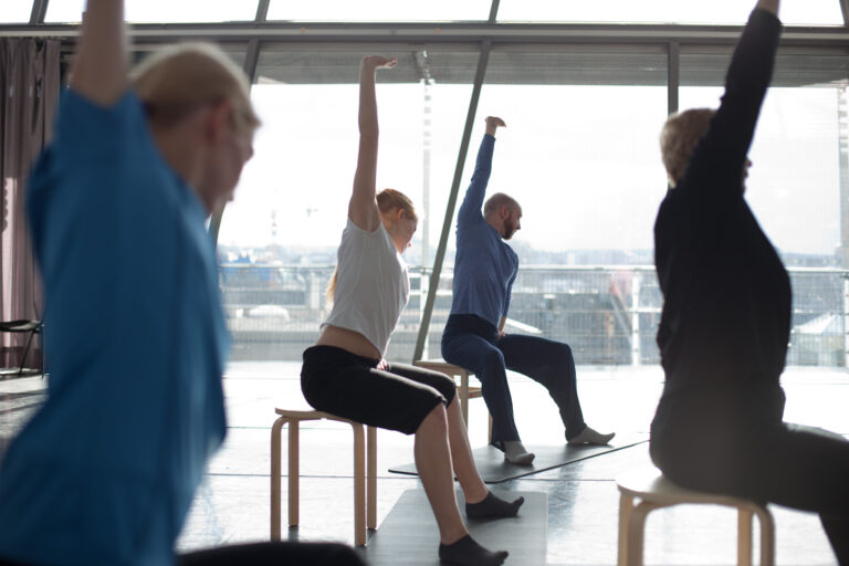 Clients extend their arms in a group class in front of a large window.