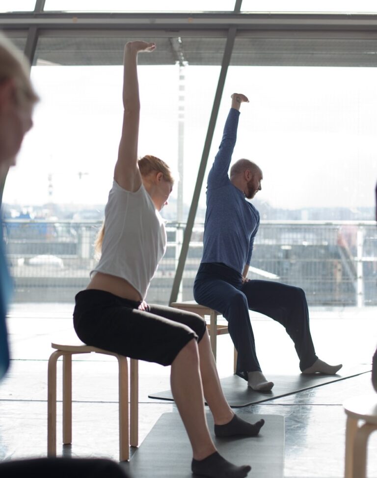 Clients sit on stools and extend their arms upwards in a backbend.