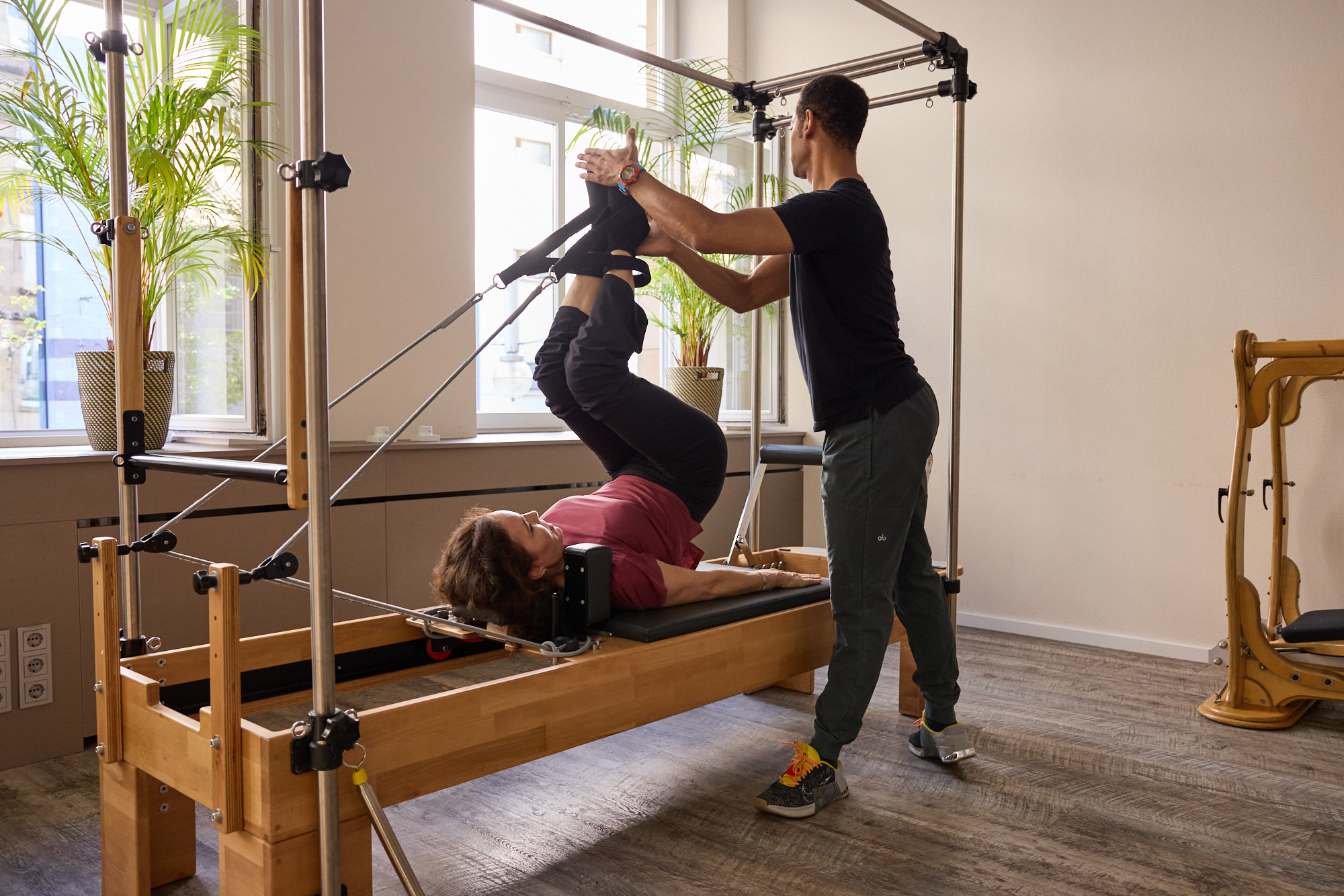 Trainer unterstützt eine Klientin bei einer Beinübung auf dem Pilates Reformer Cadillac