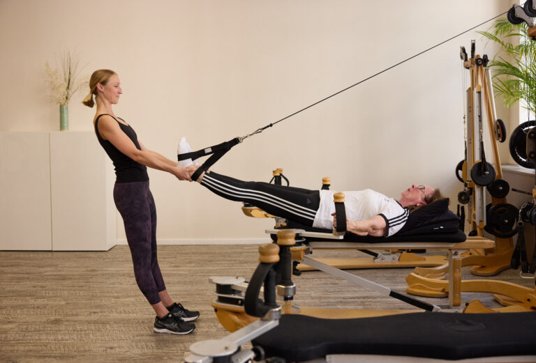 A trainer assists a client lying down with a leg exercise on the Gyrotonic machine.
