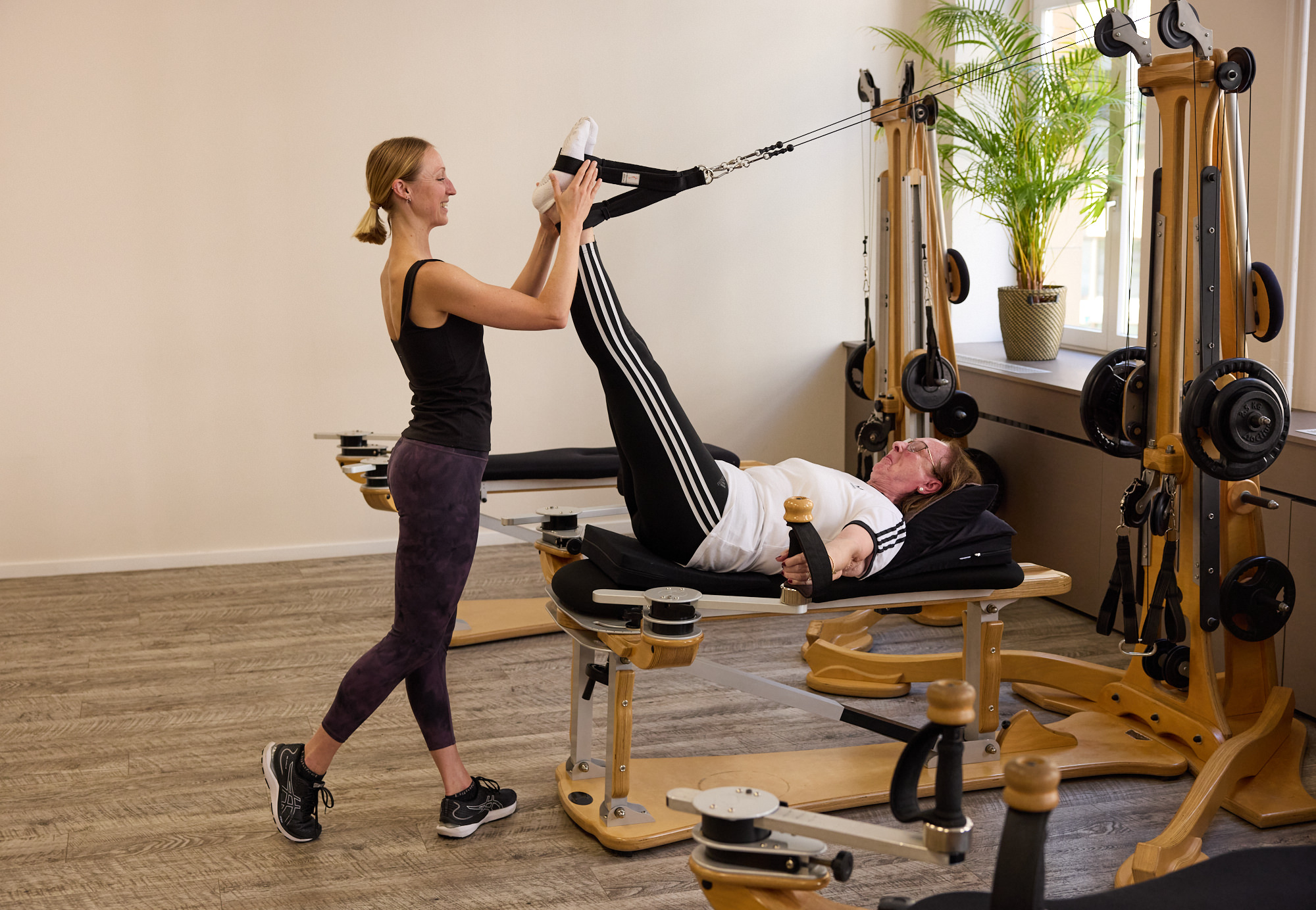 A trainer assists an older female client with a leg exercise on the Gyrotonic Pulley Tower – over-60s training.