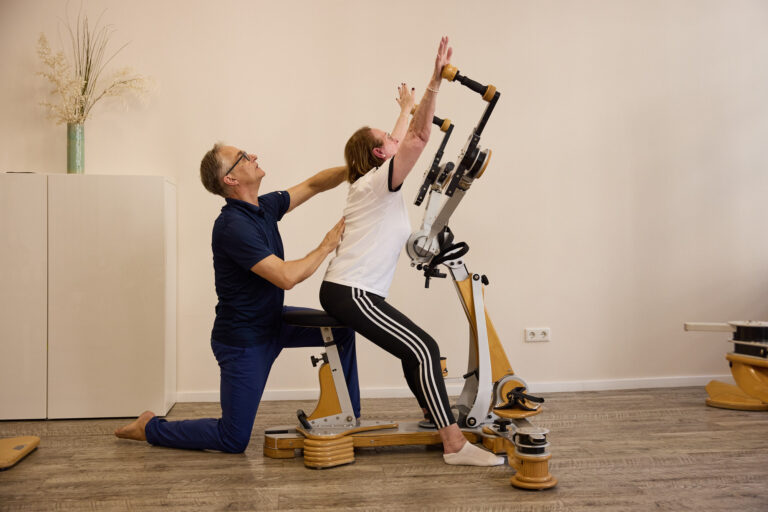 A trainer assists a client with an arm-raising stretch exercise on the Gyrotonic machine.