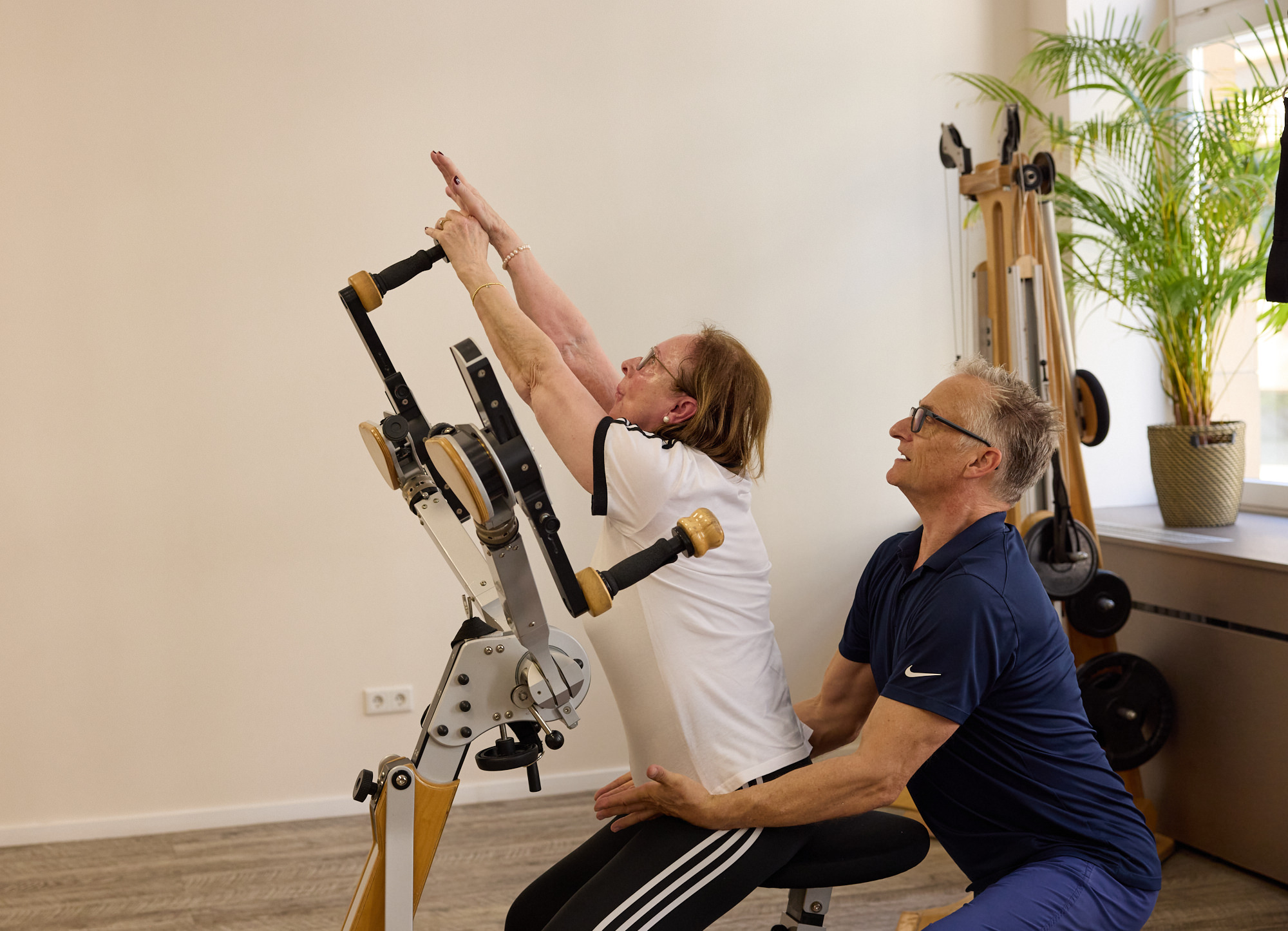 Trainer unterstützt eine Klientin bei einer Streckübung am Gyrotoner – Rehabilitation nach Operation