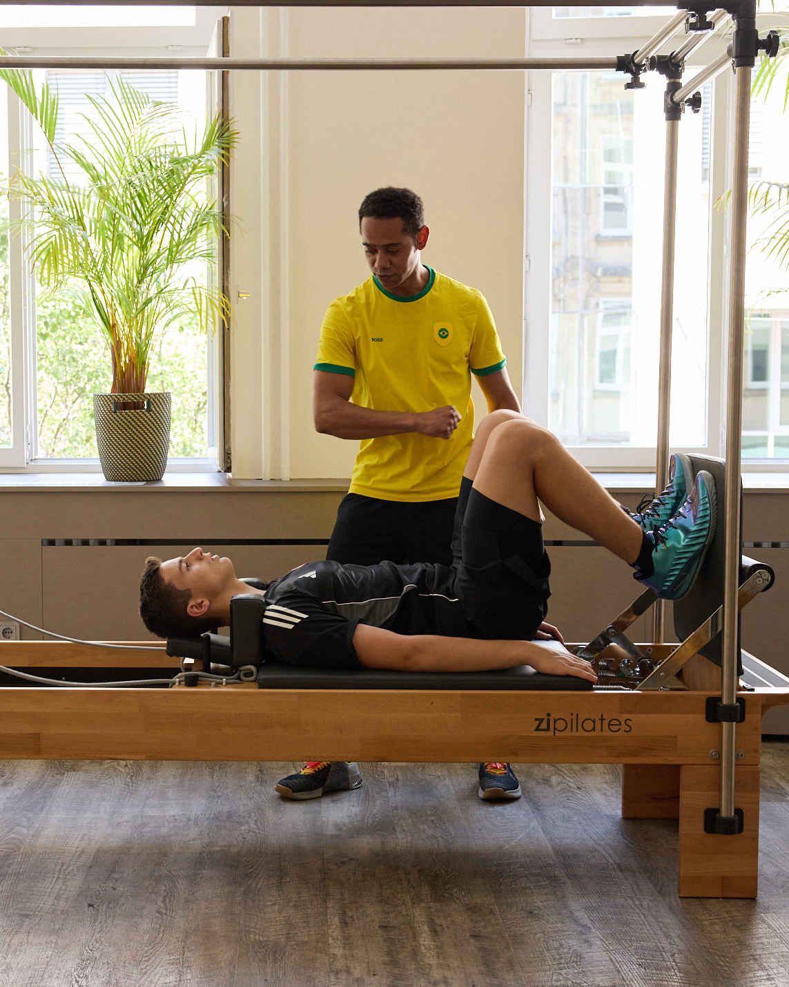 Trainer betreut einen liegenden Klienten auf dem Pilates-Reformer
