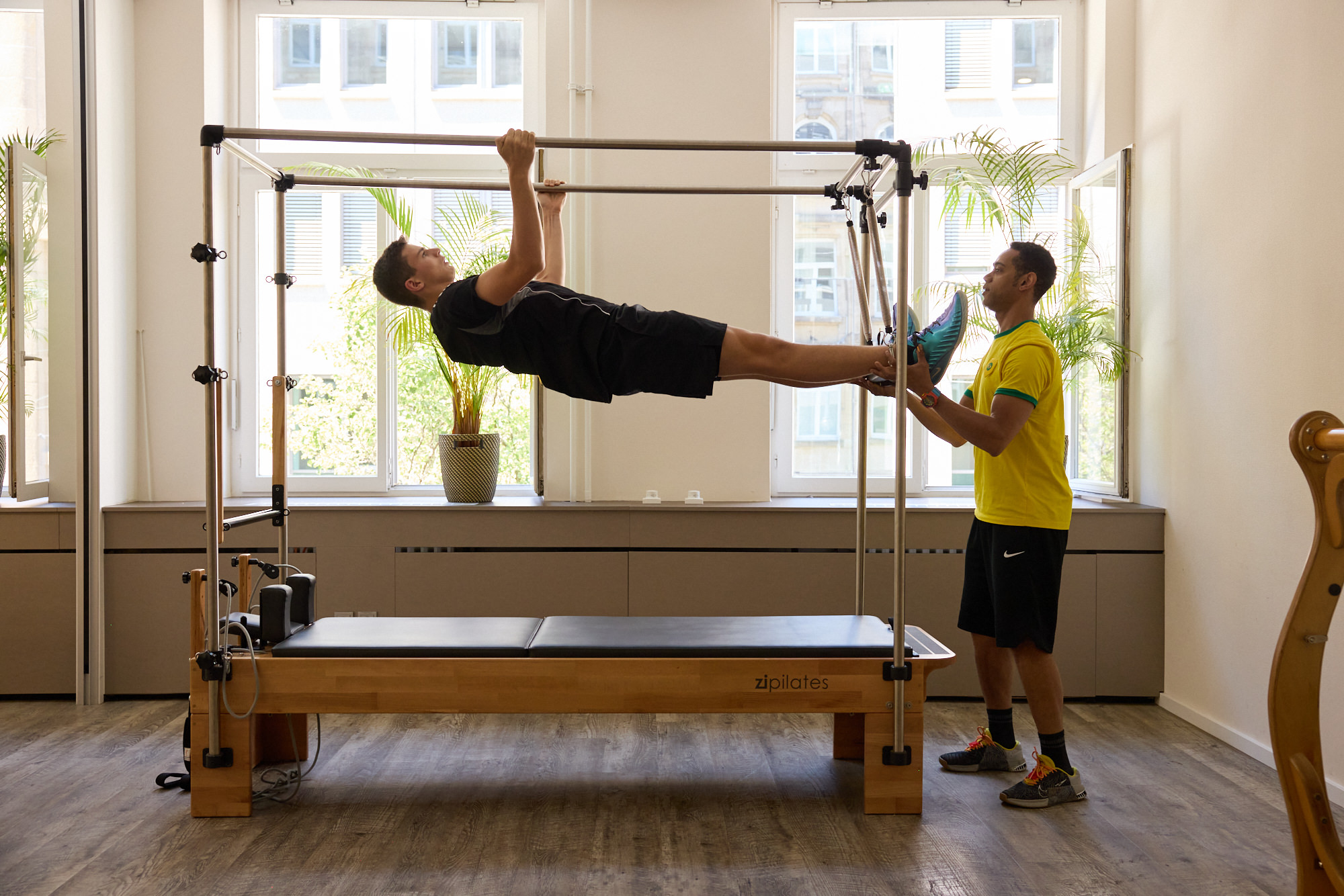 Trainer unterstützt einen Klienten bei einer Körperspannungs-Übung am Pilates Cadillac Reformer.