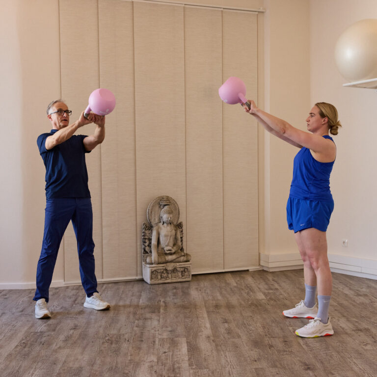 Trainer und Klientin trainieren gemeinsam mit Kettlebells im Studio – individuelles Präventionstraining