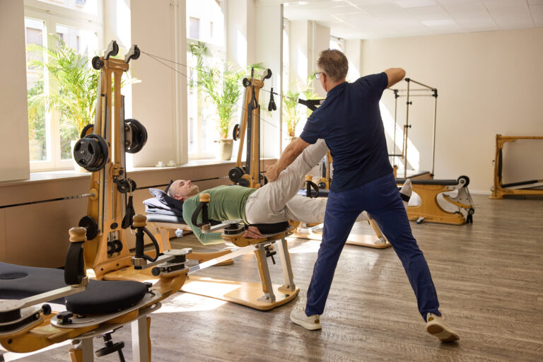 Trainer guides the leg of a client lying on the Gyrotonic machine.
