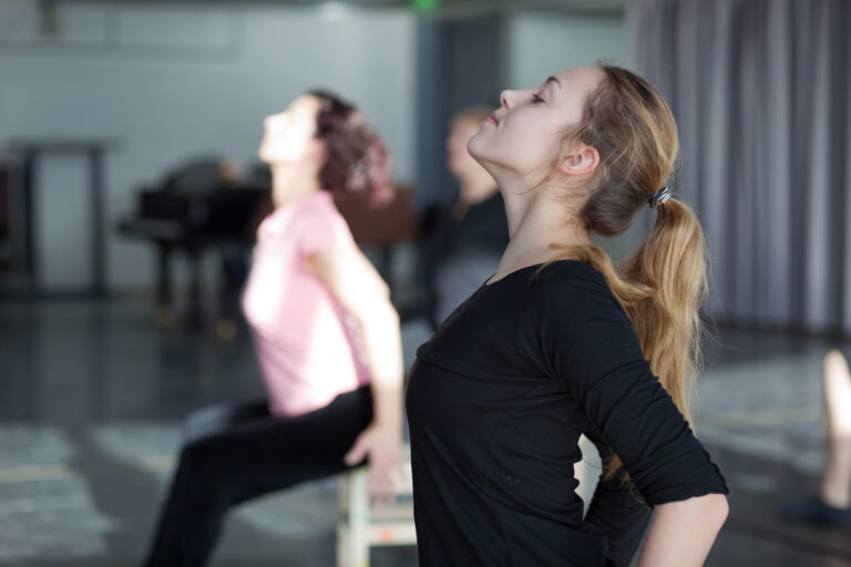 Woman leans her head back in a backward bend; other female clients in the background.